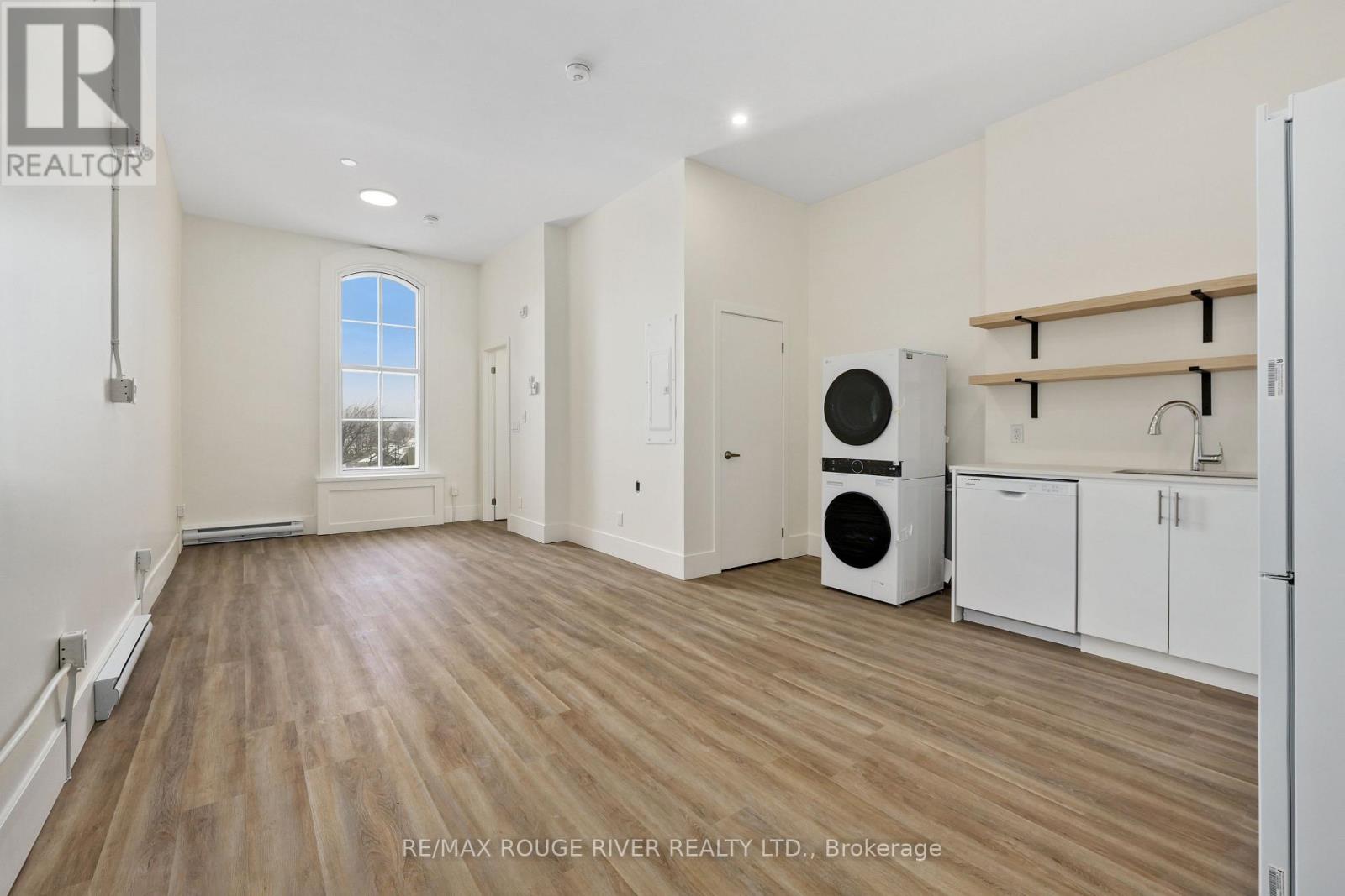 A spacious room with wooden flooring and white walls, featuring a window, a washing machine, and a dryer.