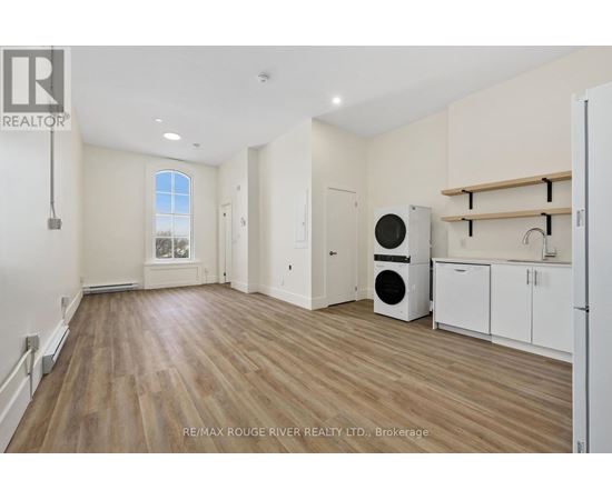 A spacious room with wooden flooring and white walls, featuring a window, a washing machine, and a dryer.
