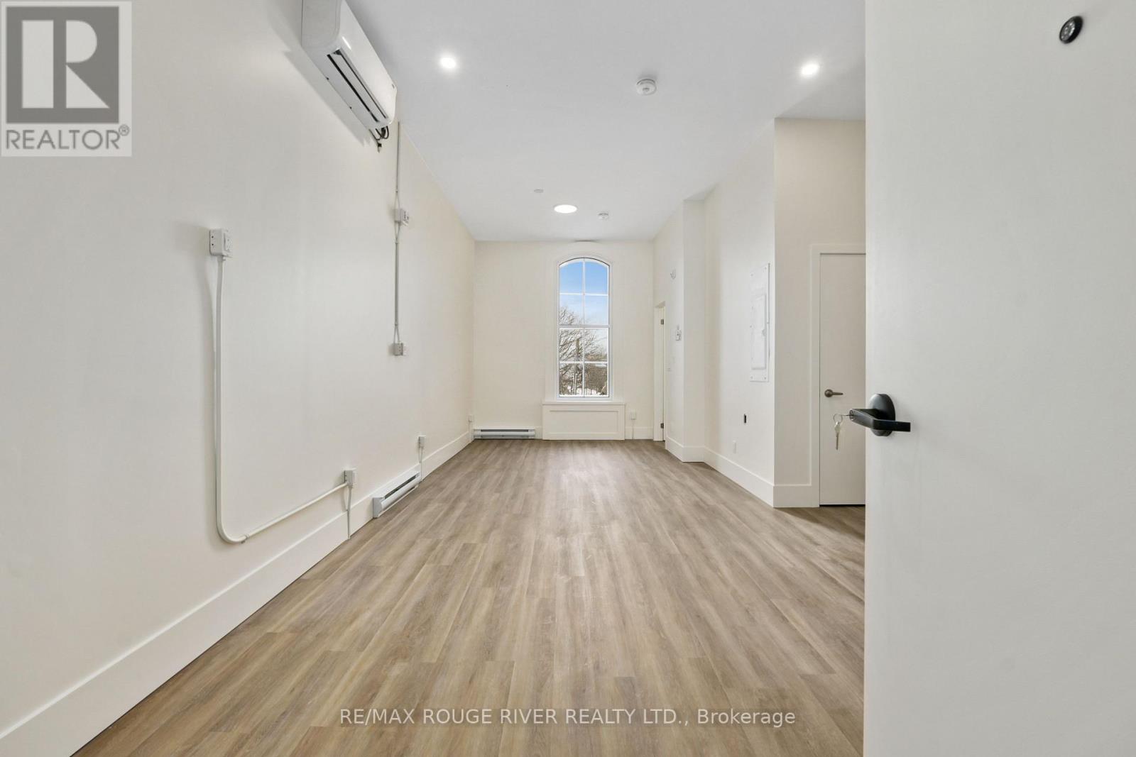 A spacious room with wooden floors and white walls, with a door on the right side.