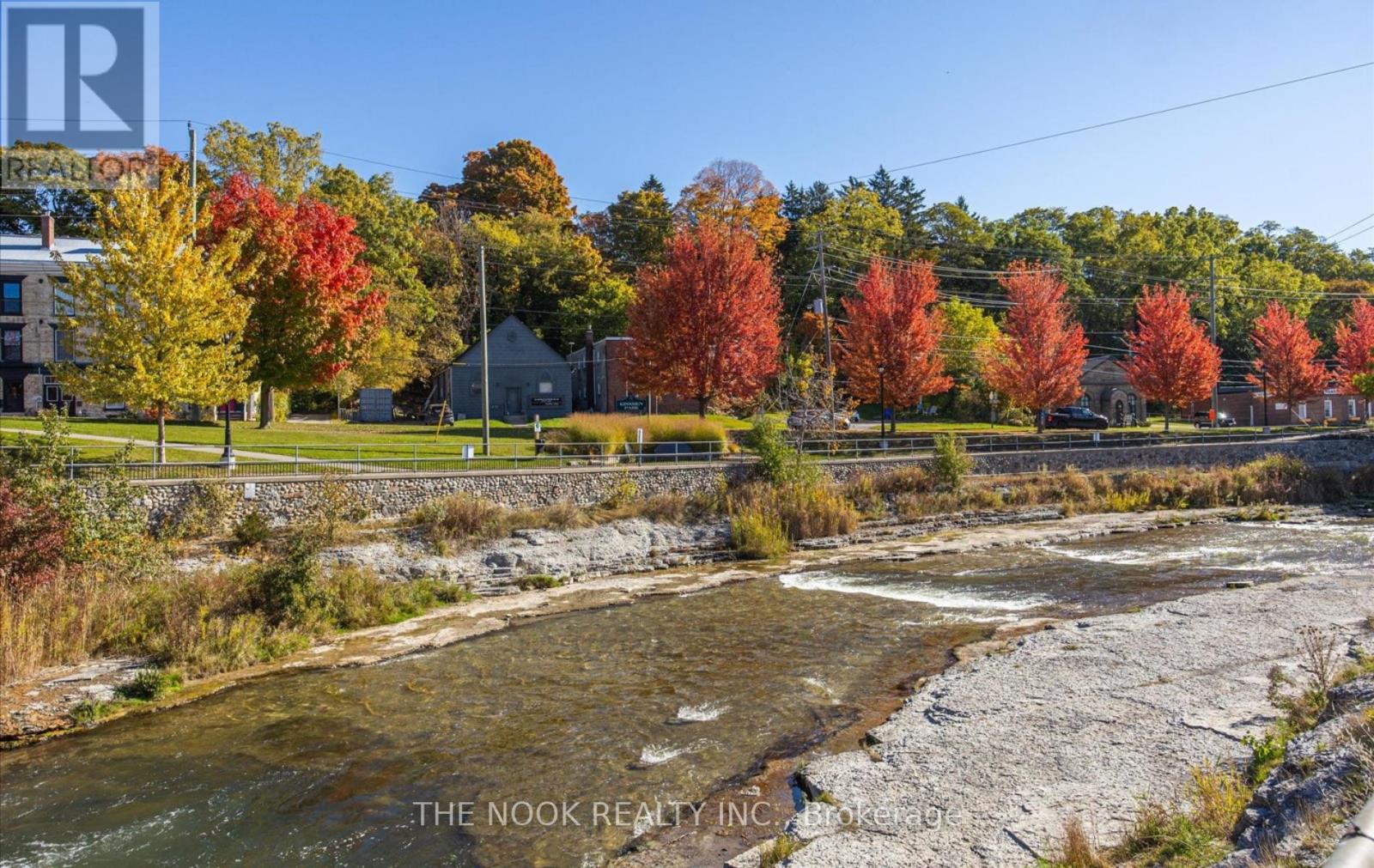 A river flows through a rocky bed with autumn trees in the background.