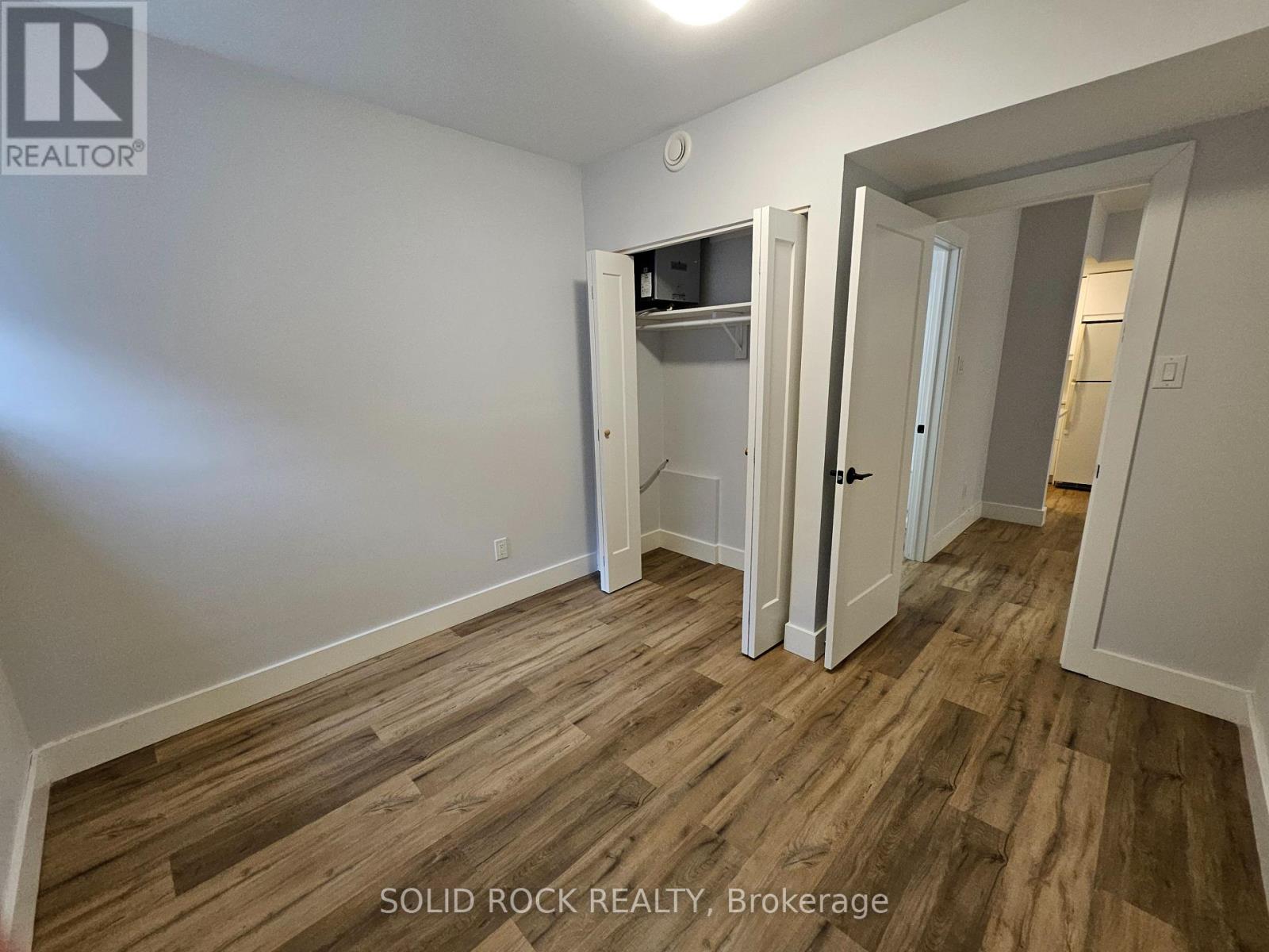 A room with wood flooring and white walls, with a closet and a doorway leading to another room.