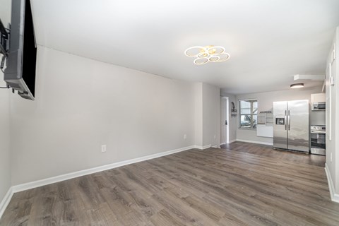 A living room with a television on the wall and a kitchen in the background.