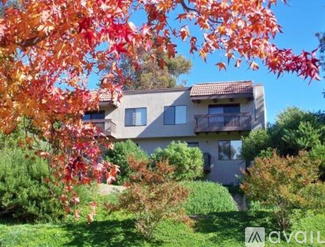 A house with a balcony is surrounded by greenery and trees with red leaves.