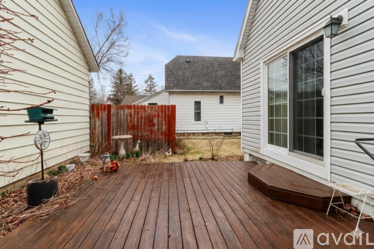 A wooden deck in front of a white house with a red fence.