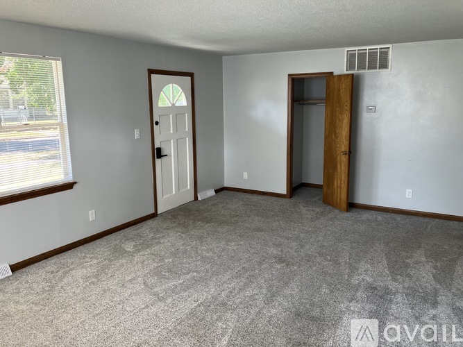A room with a carpeted floor, two doors, and a window with blinds.