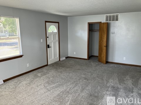 A room with a carpeted floor, two doors, and a window with blinds.