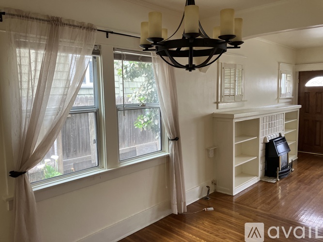A living room with a chandelier, a window with curtains, and a bookshelf.