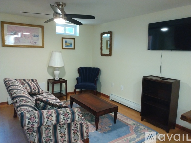 A living room with a striped couch, a blue chair, a lamp, a ceiling fan, a flat screen TV, and a rug.