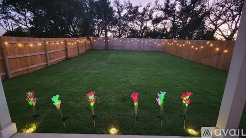 A backyard with a wooden fence and artificial grass with four colorful flowers in the middle.