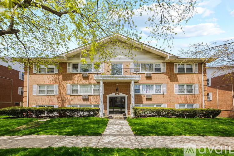 A brick apartment building with a front lawn and trees.
