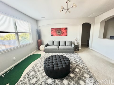 A living room with a grey couch, a black ottoman, and a red flower painting on the wall.