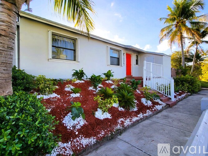 A house with a red door and a white fence surrounded by green plants.