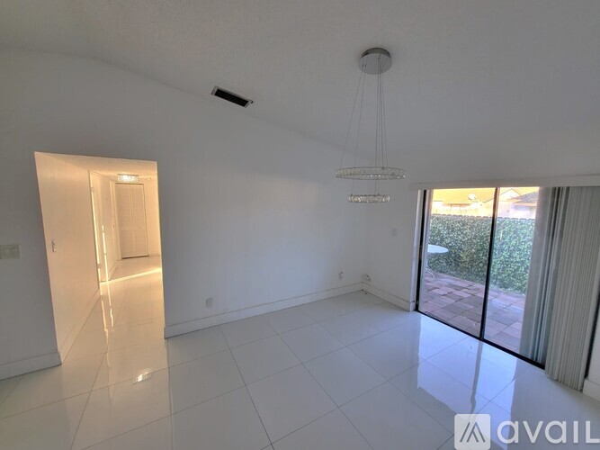 A spacious room with white tiled flooring and a chandelier hanging from the ceiling.