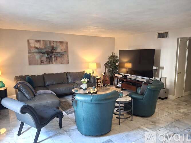 A living room with a grey sofa, a black leather chair, a green armchair, a small table with a vase of flowers, and a television.