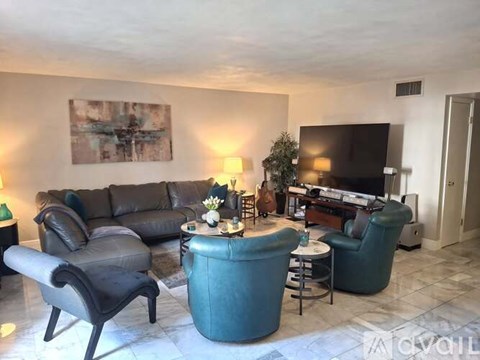 A living room with a grey sofa, a black leather chair, a green armchair, a small table with a vase of flowers, and a television.
