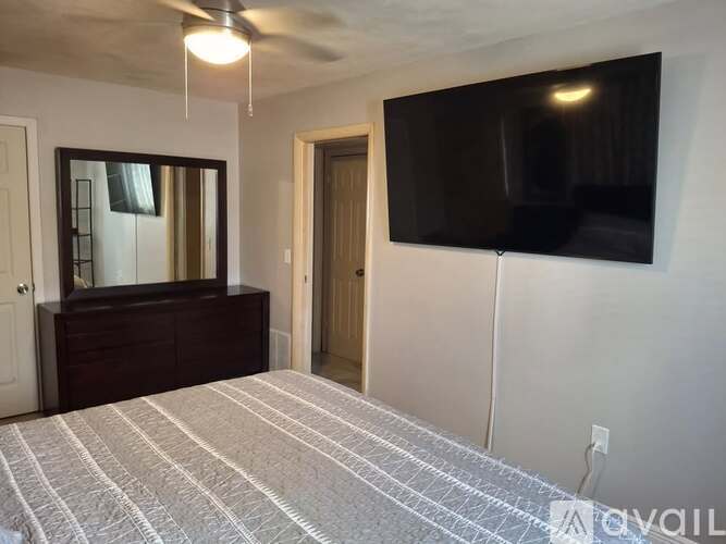 A bedroom with a bed, dresser, mirror, and a flat screen TV mounted on the wall.