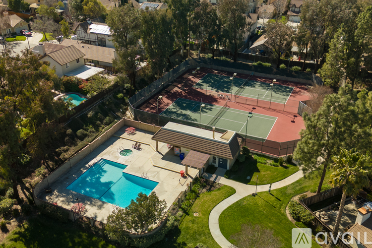 A tennis court is surrounded by a pool and a house.