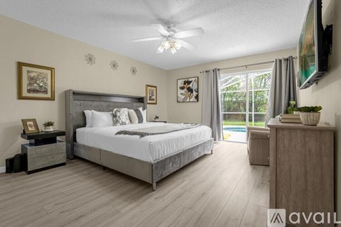 A bedroom with a large bed, a ceiling fan, and a nightstand with a lamp.