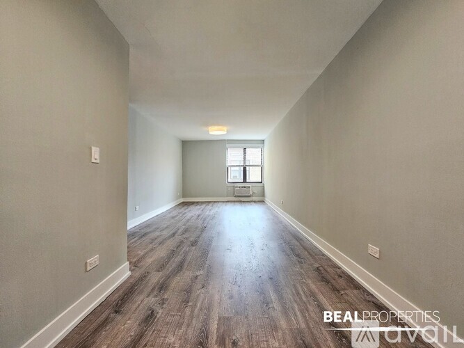A long hallway with wood flooring and a window at the end.