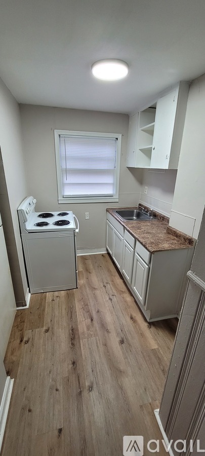 A kitchen with a white stove top oven and wooden flooring.