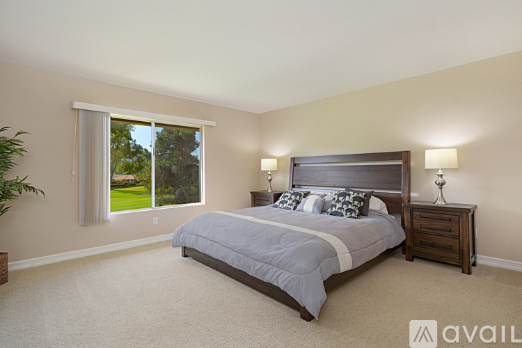 A bedroom with a large bed and a window overlooking a green lawn.