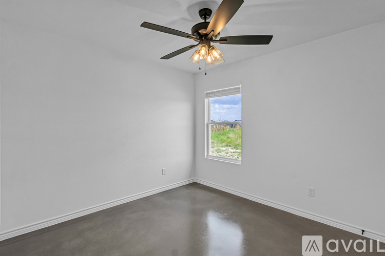 A room with a ceiling fan and a window showing a view of a grassy area outside.