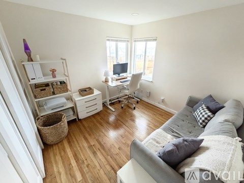 A living room with a grey couch and a white desk with a computer.