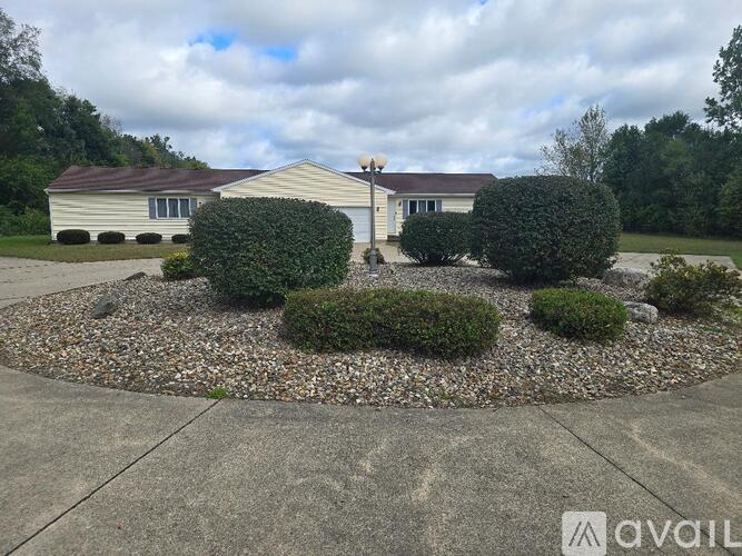 A house with a grey roof and a grey garage door is surrounded by a gravel garden bed with bushes.