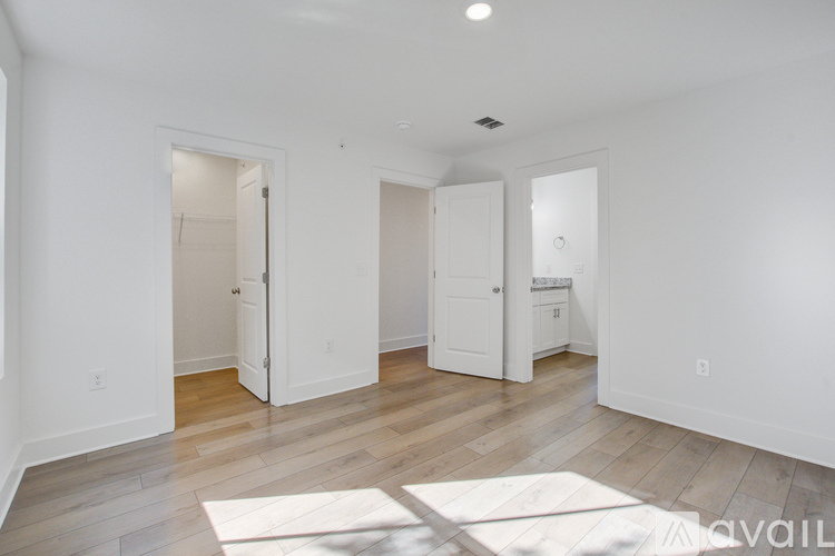 A spacious room with white walls and wooden flooring, featuring a large open doorway and a white mat on the floor.