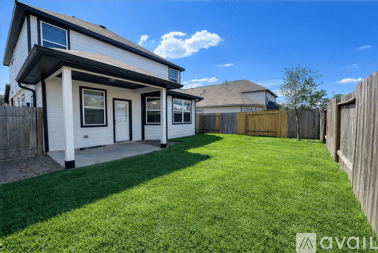 A house with a white exterior and a black roof is surrounded by a wooden fence and has a green lawn.
