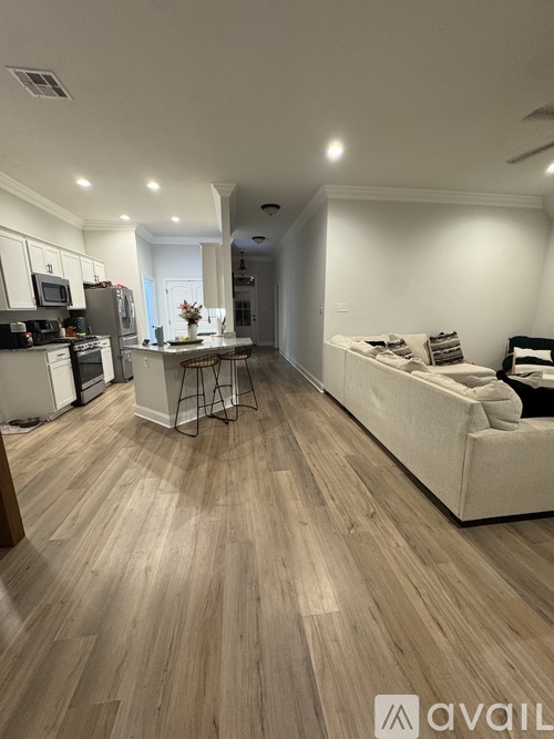 A living room with a white couch and a kitchen area with white cabinets.