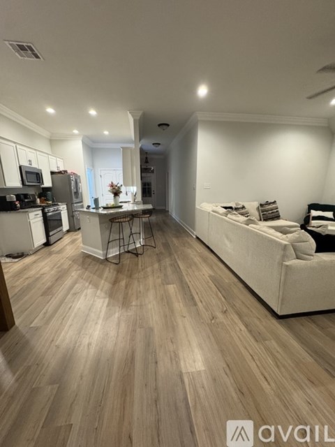 A living room with a white couch and a kitchen area with white cabinets.