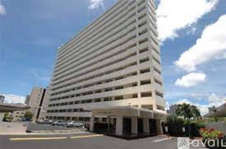 A tall white building with a parking lot in front.