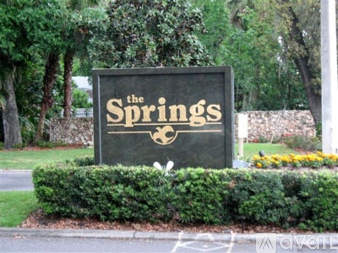 A sign that says "The Springs" is in front of a hedge.