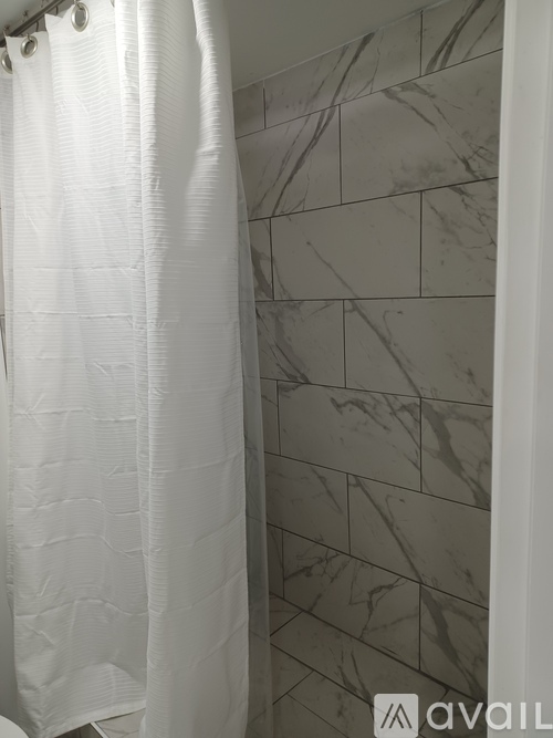 A white shower curtain hangs in front of a marble tiled shower wall.