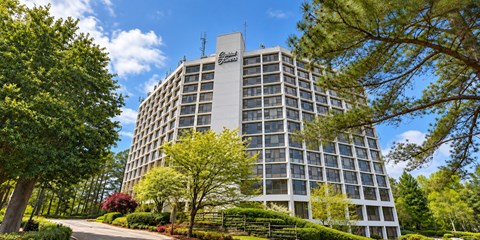 A tall building with a sign on the top is surrounded by trees.