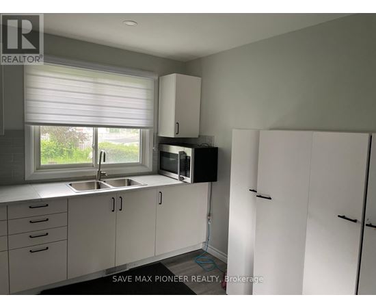 A kitchen with white cabinets and a window with blinds.