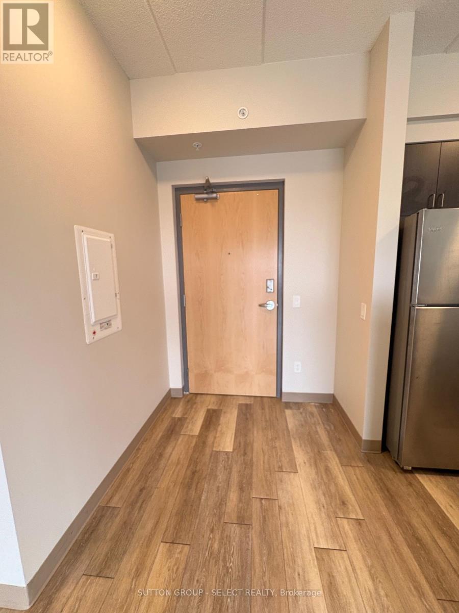 A hallway with a wooden floor and a metal refrigerator on the right.