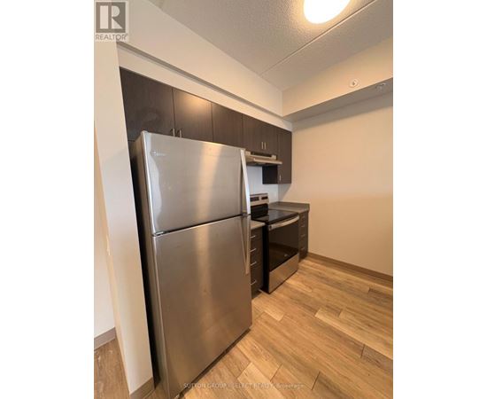 A stainless steel refrigerator in a kitchen with wooden flooring.