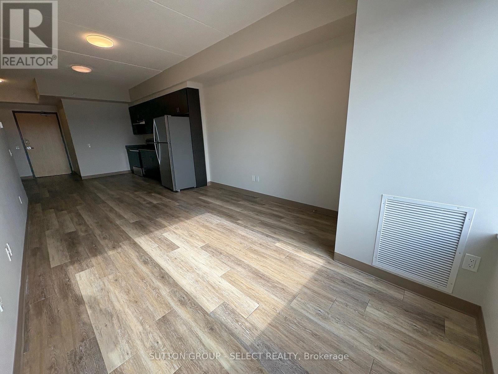 A spacious room with wooden flooring and a refrigerator in the corner.