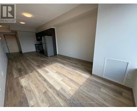 A spacious room with wooden flooring and a refrigerator in the corner.