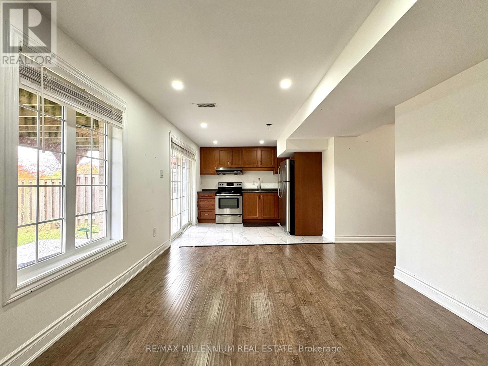 A spacious room with wooden flooring and a kitchen area in the background.