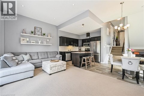 A well-lit, modern living room with a grey sofa and a kitchen area in the background.