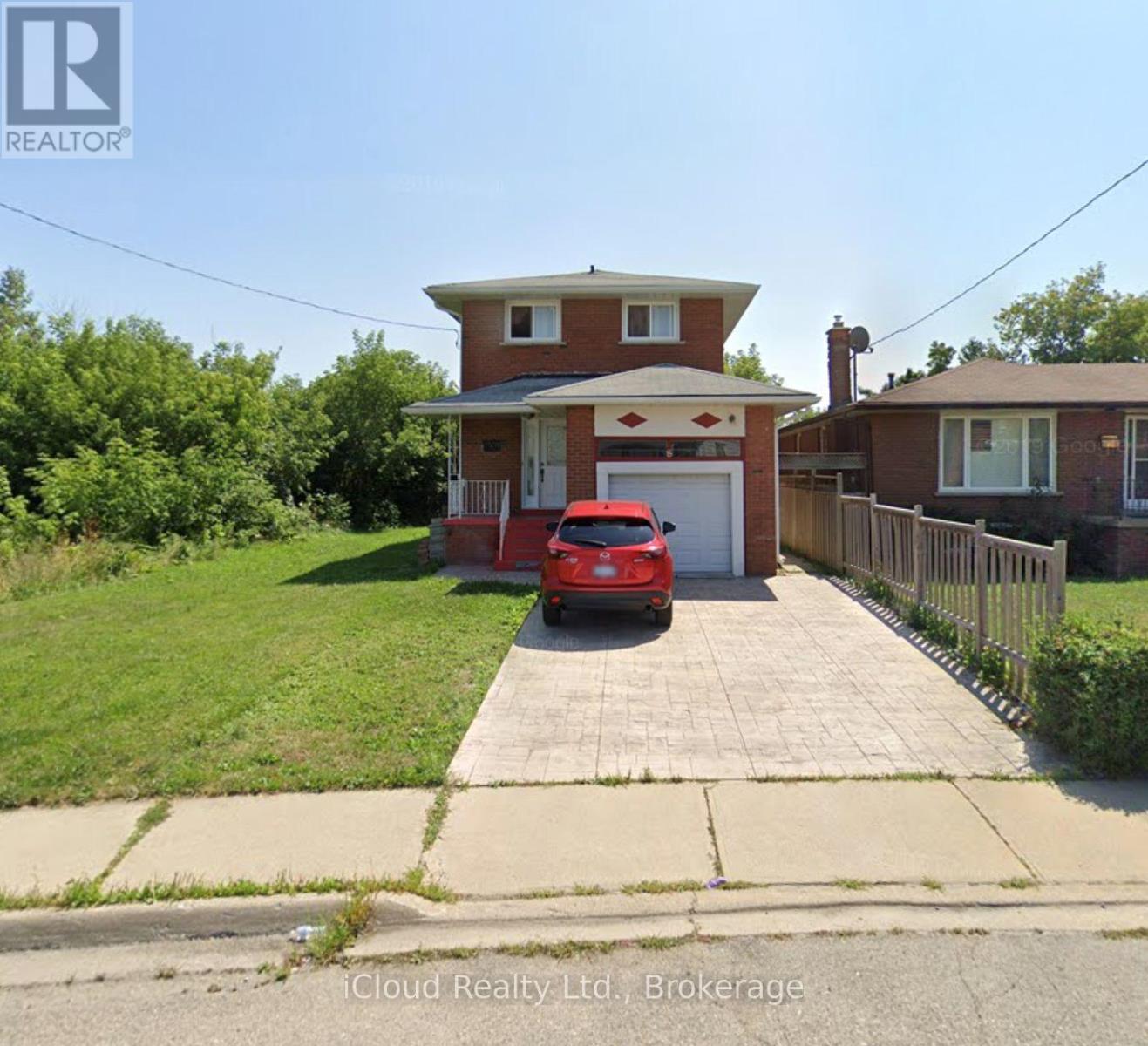 A red car is parked in front of a house with a realtor logo.