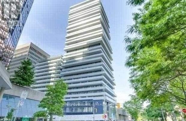 A tall, modern building with a glass facade stands in front of a tree.