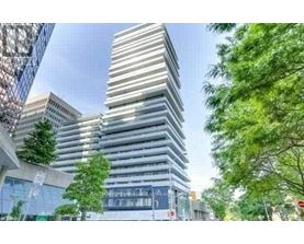 A tall, modern building with a glass facade stands in front of a tree.