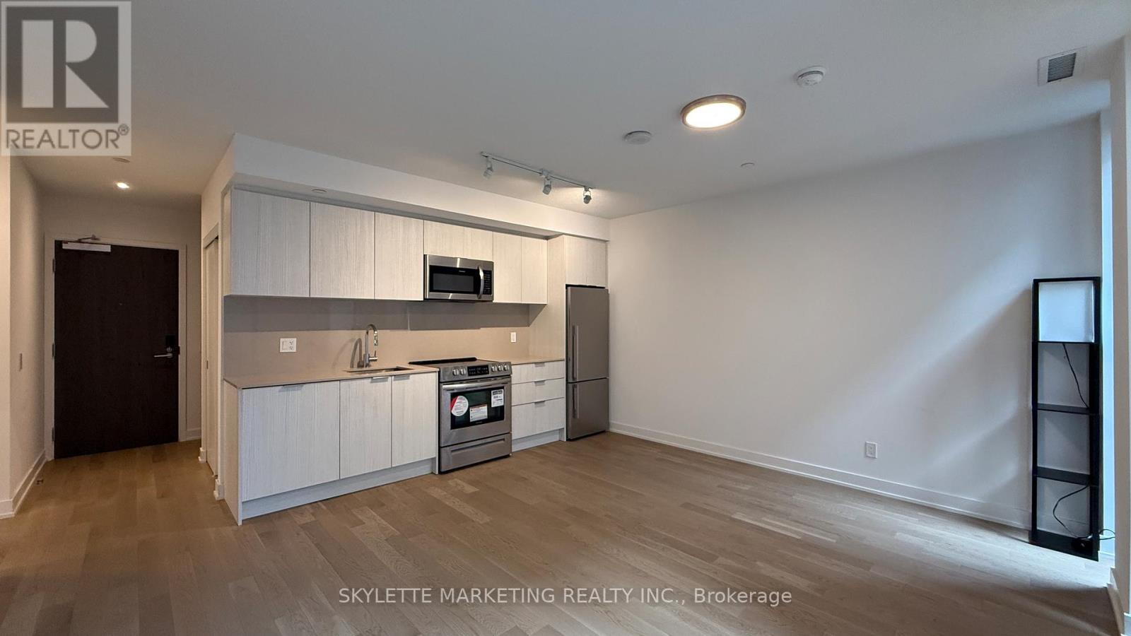 A well-lit, empty room with a kitchenette and a television.
