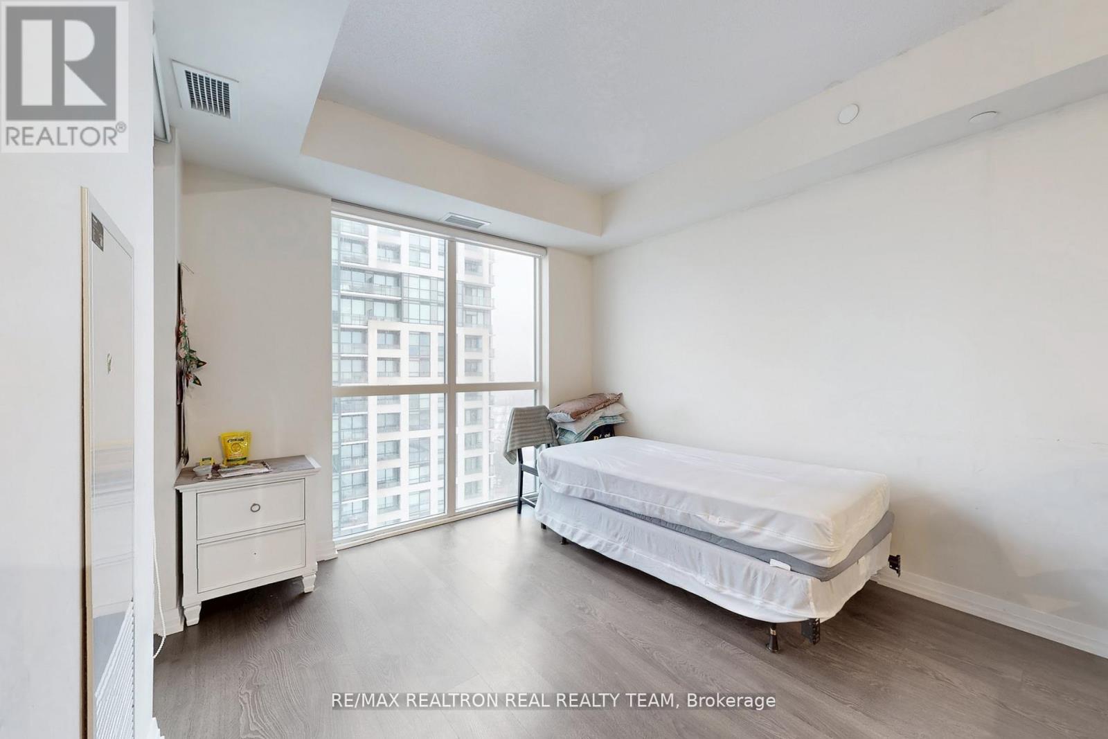 A bedroom with a bed, nightstand, and a window with a view of a building outside.