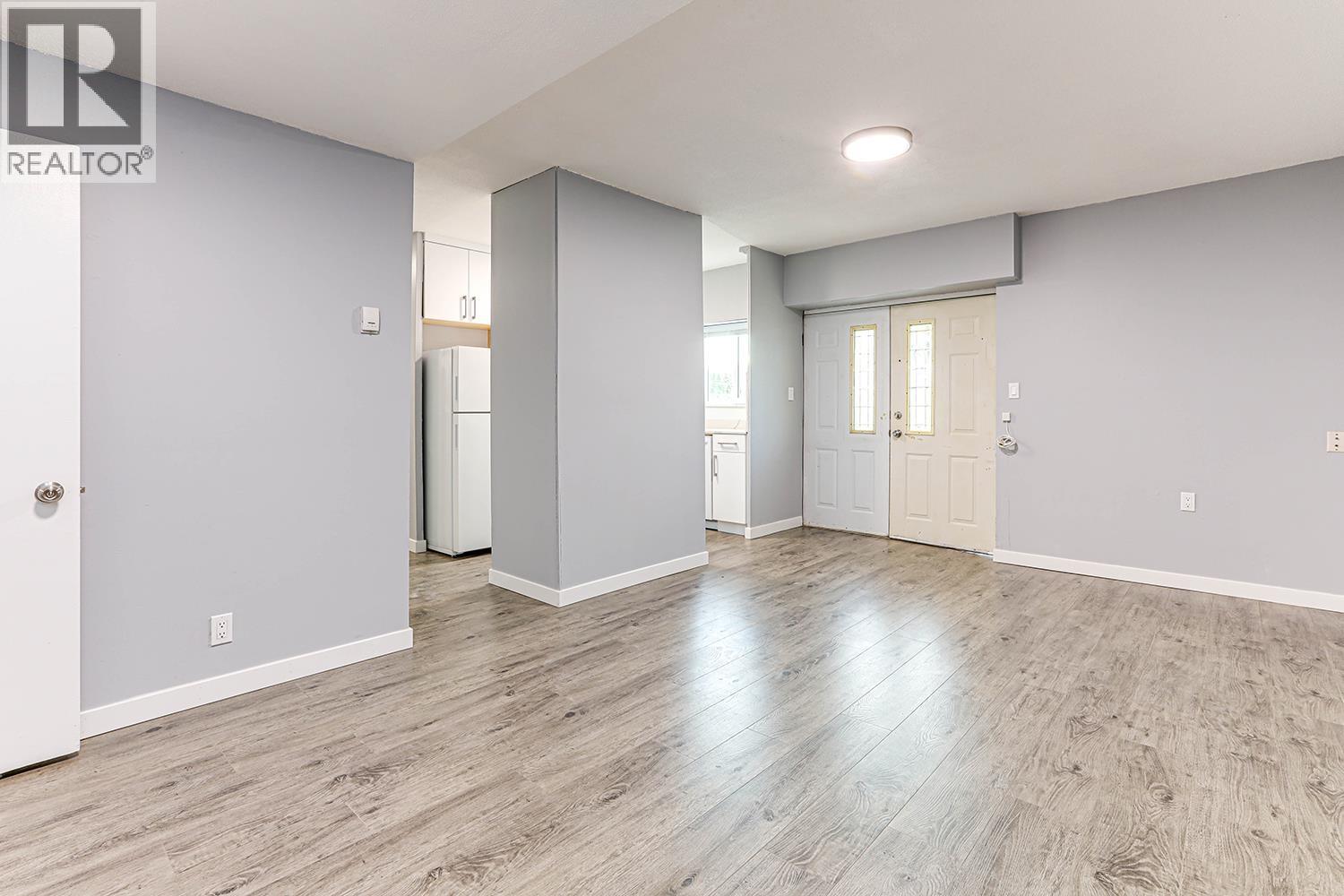 A spacious room with light grey walls and wooden flooring.