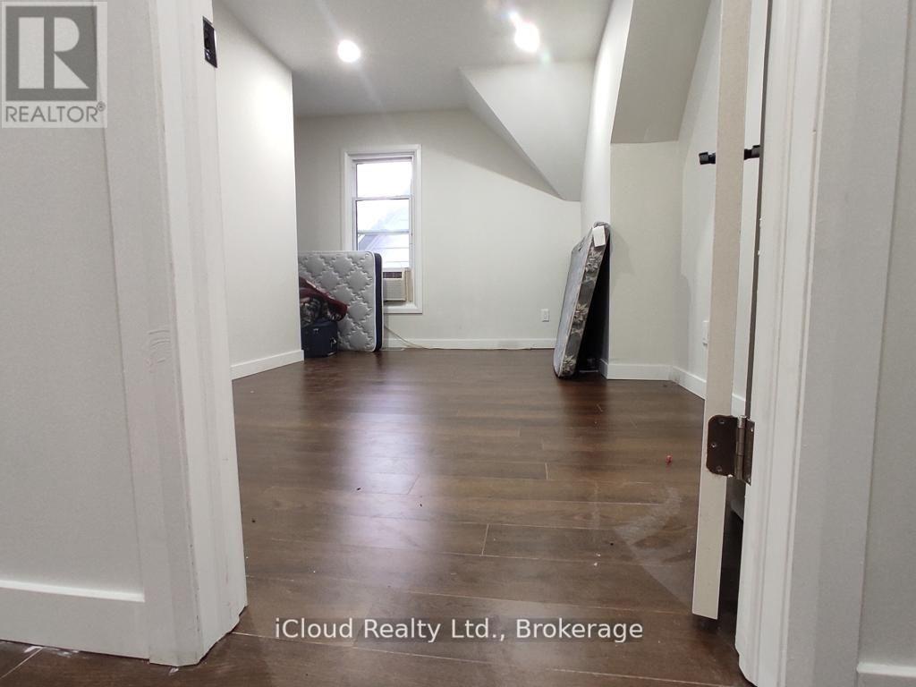 A room with white walls and wooden flooring, with a mattress and box spring in the corner.